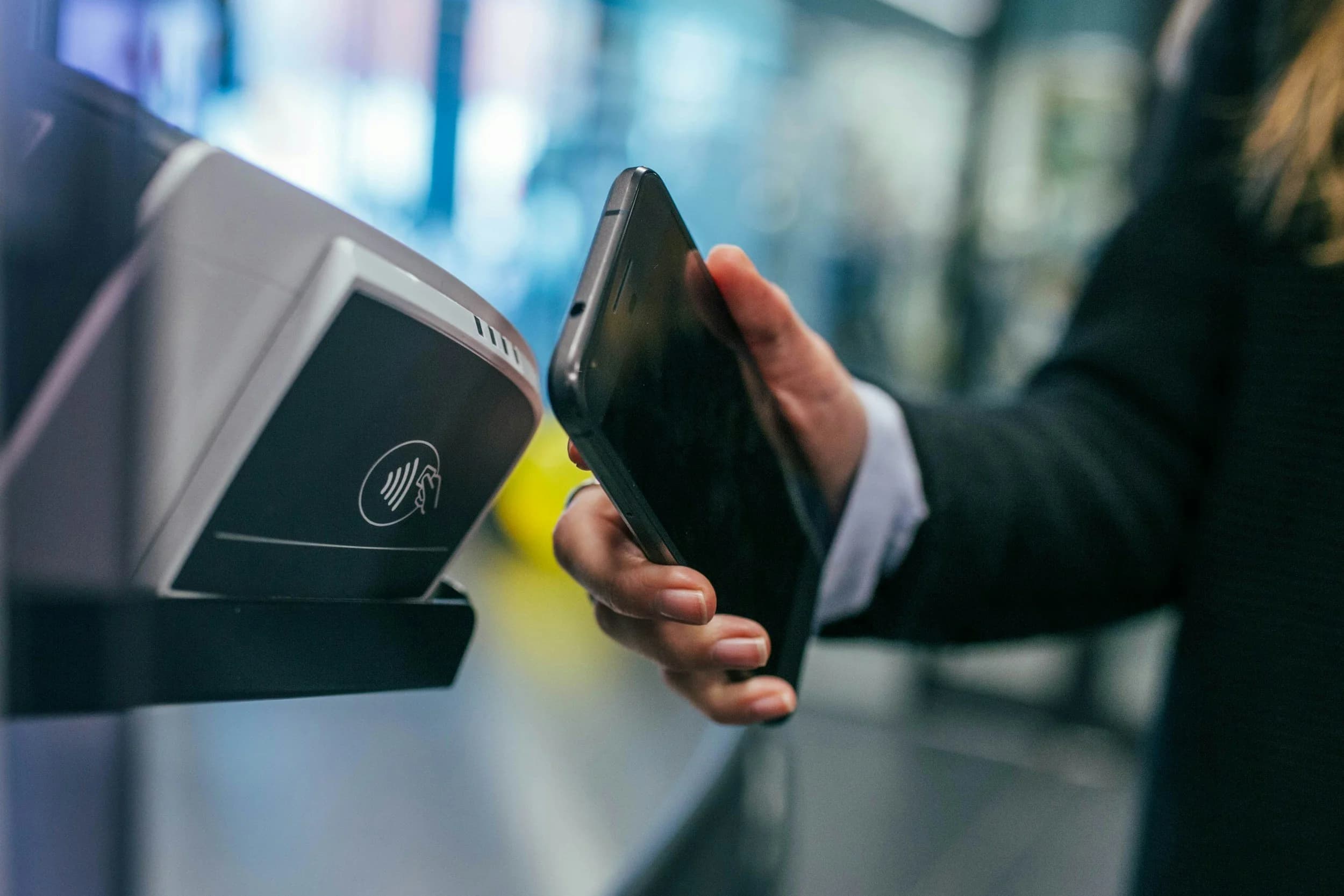 A hand holding a phone against a contactless payment terminal.