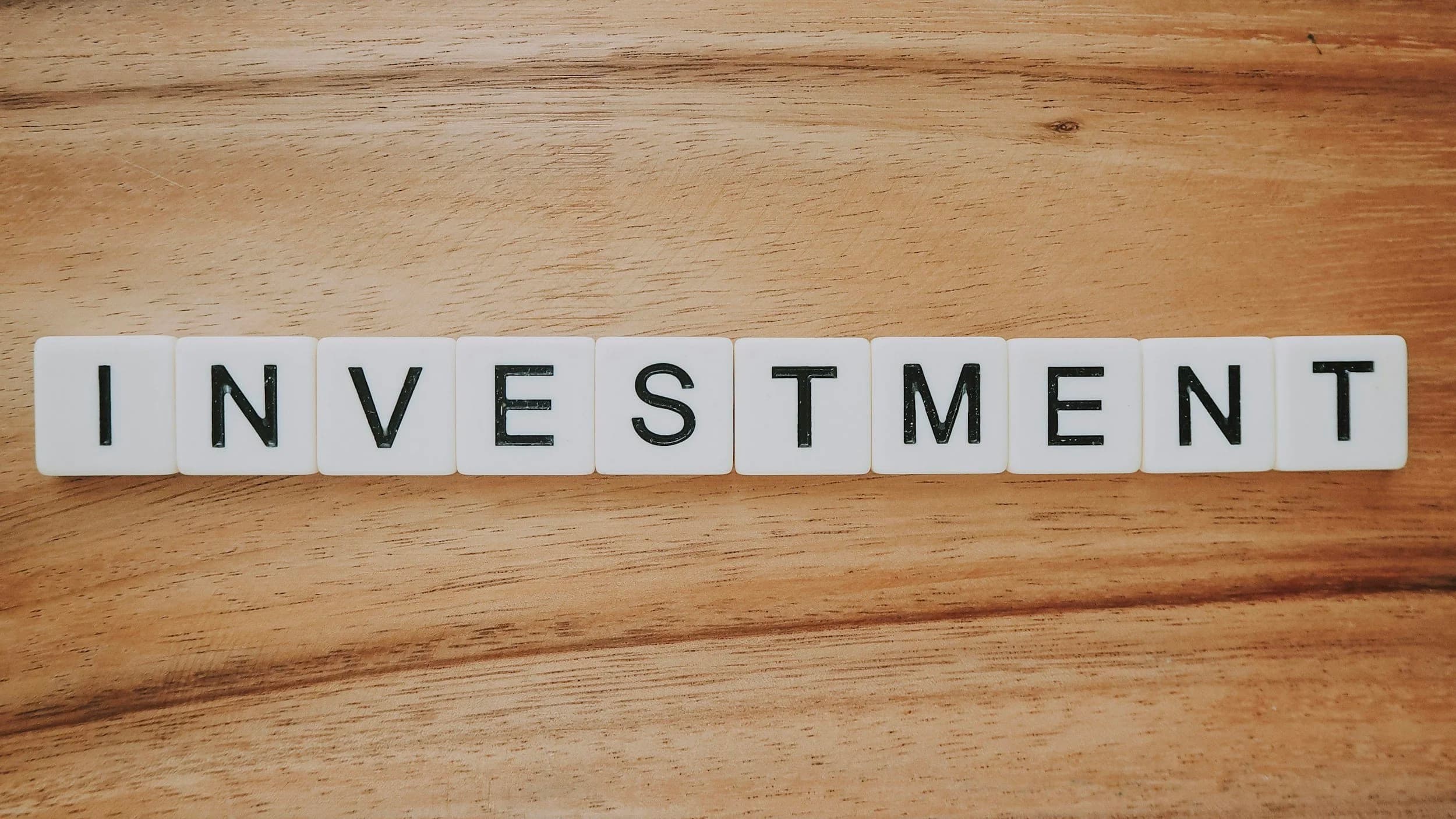 Letter tiles lined up on wood, spelling out the word “INVESTMENT”.