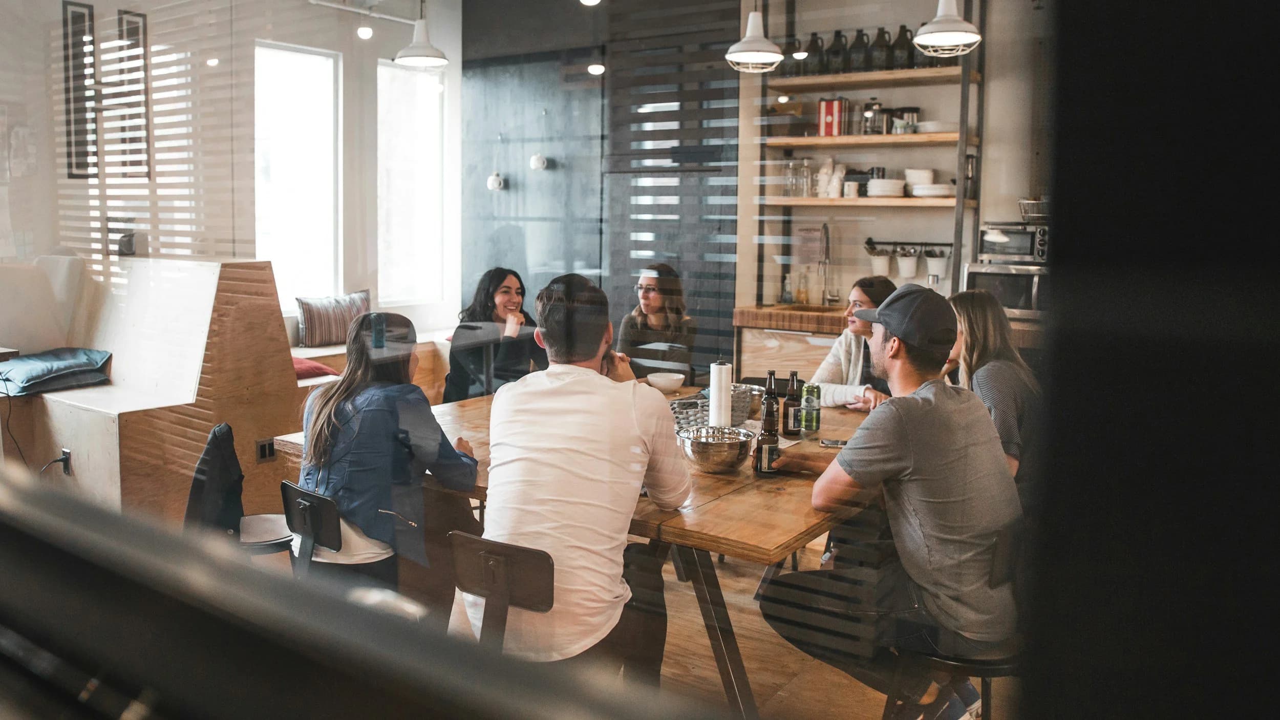 Sept personnes assises autour d'une longue table en bois dans un espace de coworking.